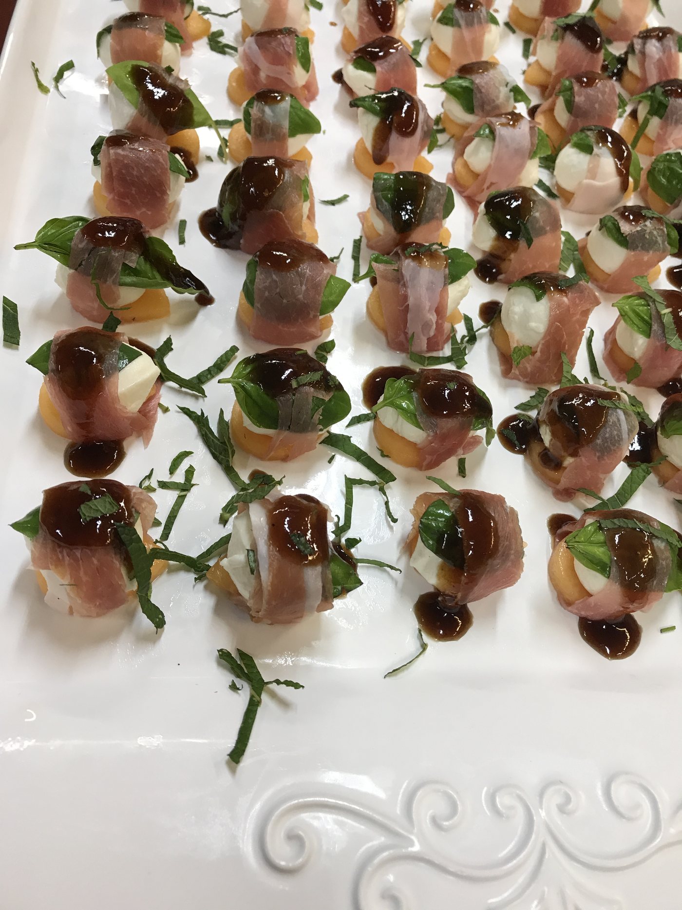 Prosciutto-melon bites on a white platter